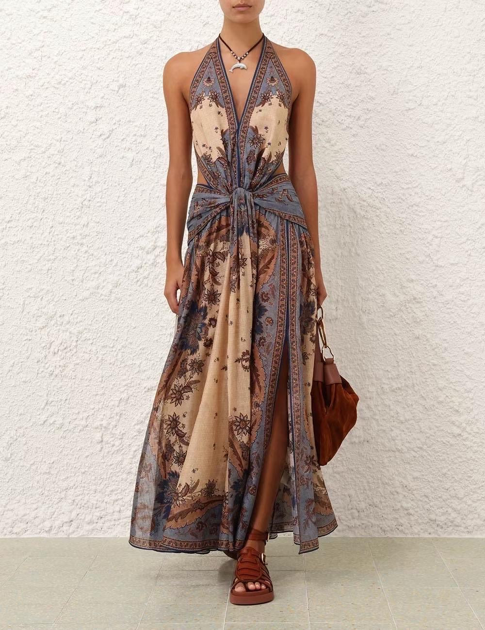 Vestido largo sin mangas, con cuello halter y nudo delantero a la altura de la cintura. Presenta un diseño fluido con abertura frontal y estampado tipo bohemio en tonos beige, marrón y azul grisáceo
