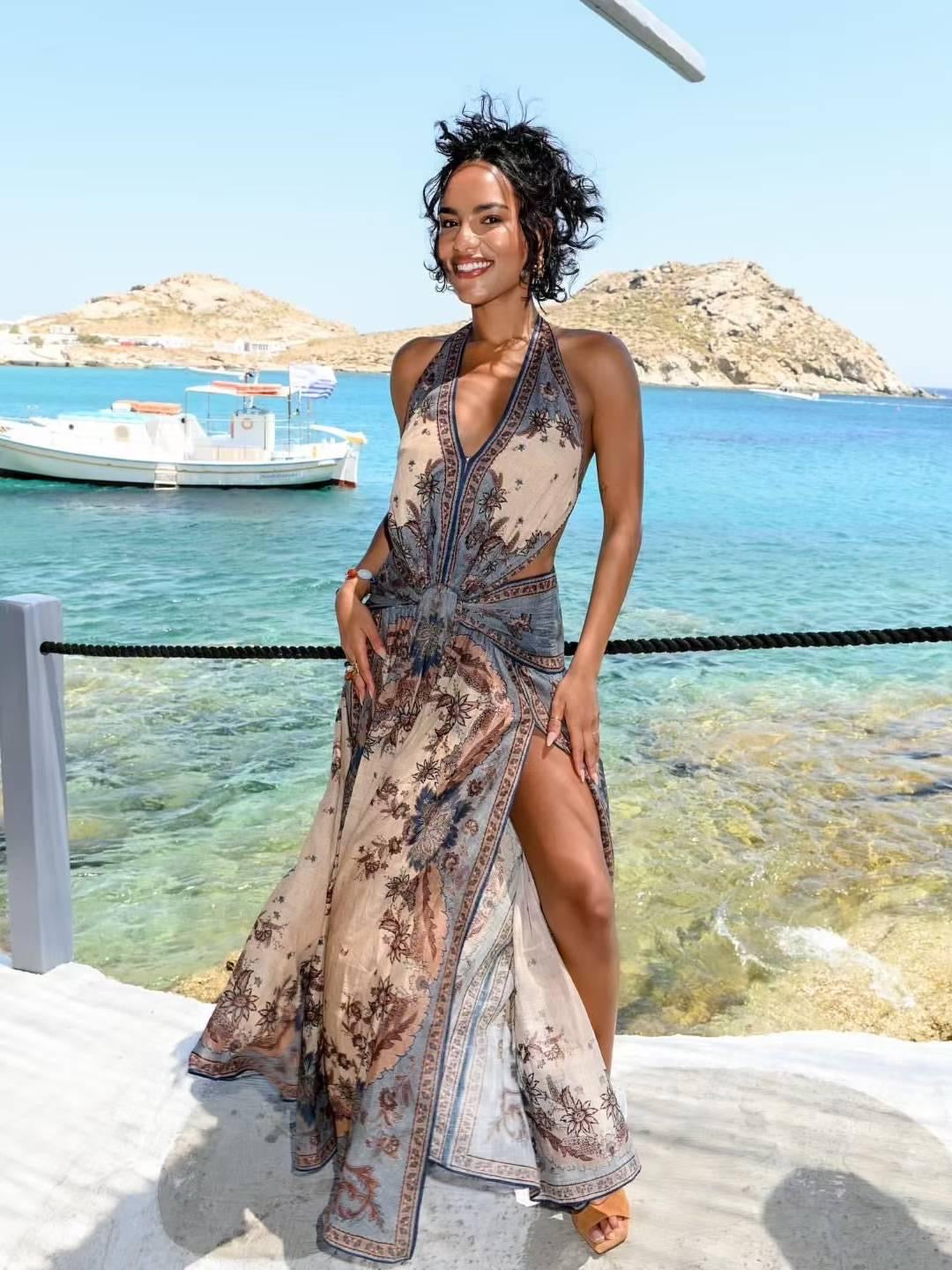 Vestido largo sin mangas, con cuello halter y nudo delantero a la altura de la cintura. Presenta un diseño fluido con abertura frontal y estampado tipo bohemio en tonos beige, marrón y azul grisáceo